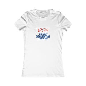 May include: A white short-sleeved t-shirt featuring a graphic on the chest. The graphic displays a digital clock showing 12:34 in red text inside a thin rectangular border, with the blue text THE MOST SEQUENTIAL TIME OF DAY printed below it.