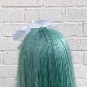 Puede incluir: Una pinza para el pelo de color blanco con dos flores de orqu&iacute;dea blancas. La pinza para el pelo est&aacute; en una peluca de color turquesa.