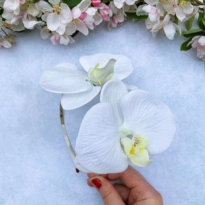 Puede incluir: Una diadema con una flor de orqu&iacute;dea blanca sobre un fondo blanco.