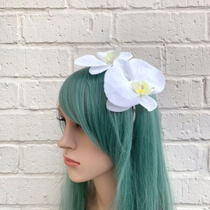 Puede incluir: Pinza para el pelo de orqu&iacute;dea blanca con dos flores de orqu&iacute;dea blancas. Las flores est&aacute;n hechas de tela y tienen un aspecto realista.
