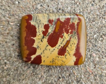 Pode incluir: Uma pedra polida, retangular, com um padrão único de vermelho, amarelo e preto. A pedra tem um acabamento liso e brilhante.