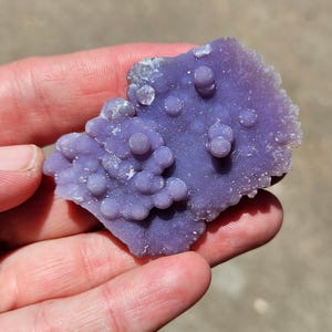May include: A close-up of a purple agate geode with a textured surface and many small, round bumps. The geode is a natural formation with a unique and beautiful pattern.