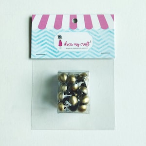 May include: A clear plastic bag containing a pack of gold-colored metal tacks with silver heads. The bag is labeled "dress my craft".
