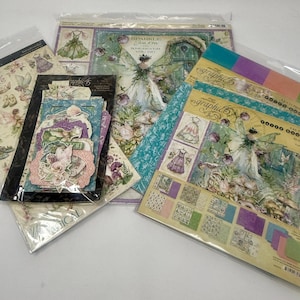 Puede incluir: Una colección de papel y adornos para álbumes de recortes con diseños de hadas y flores. Los papeles incluyen imágenes de hadas, vestidos y elementos botánicos en colores pastel. Algunos artículos están empaquetados en plástico transparente.