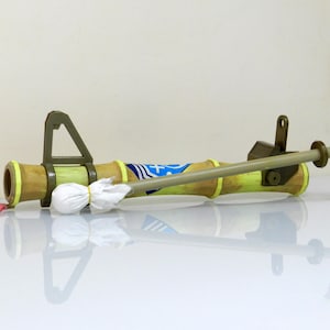 Puede incluir: Una pistola de agua de juguete verde y marr&oacute;n con un pa&ntilde;o blanco sujeto al ca&ntilde;&oacute;n. La pistola tiene un dise&ntilde;o amarillo y azul en el ca&ntilde;&oacute;n. La pistola est&aacute; tumbada sobre una superficie blanca.