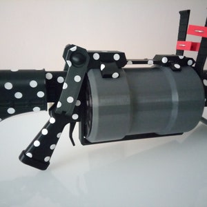 Puede incluir: Una pistola de juguete de lunares negros y blancos con un ca&ntilde;&oacute;n gris y un mango rojo y negro. La pistola est&aacute; hecha de pl&aacute;stico y tiene un dise&ntilde;o realista.