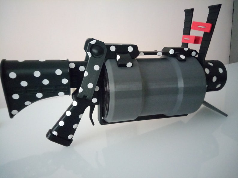 Puede incluir: Una pistola de juguete de lunares negros y blancos con un ca&ntilde;&oacute;n gris y un mango rojo y negro. La pistola est&aacute; hecha de pl&aacute;stico y tiene un dise&ntilde;o realista.