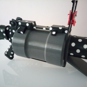 Puede incluir: Una pistola de juguete impresa en 3D de color negro y blanco con lunares y un ca&ntilde;&oacute;n gris. La pistola tiene un peque&ntilde;o clip rojo sujeto al lateral.