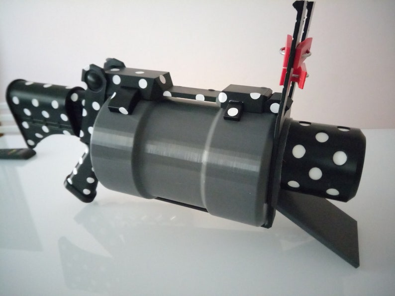 Puede incluir: Una pistola de juguete impresa en 3D de color negro y blanco con lunares y un ca&ntilde;&oacute;n gris. La pistola tiene un peque&ntilde;o clip rojo sujeto al lateral.