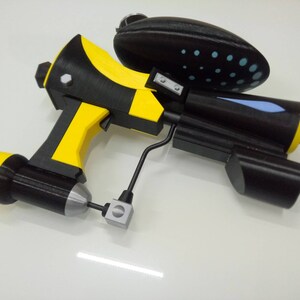 May include: A yellow and black toy gun with a blue and white detail on the barrel. The gun has a black handle and a black and white patterned grip.