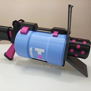 Puede incluir: Una pistola de juguete impresa en 3D con un ca&ntilde;&oacute;n azul, un mango negro y detalles en rosa. El ca&ntilde;&oacute;n tiene un patr&oacute;n de lunares negros y rosas y el texto "HEAVY" impreso en &eacute;l.