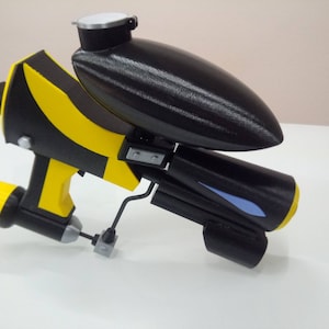 May include: A black and yellow toy gun with a blue detail. The gun has a black tank on top and a yellow barrel.