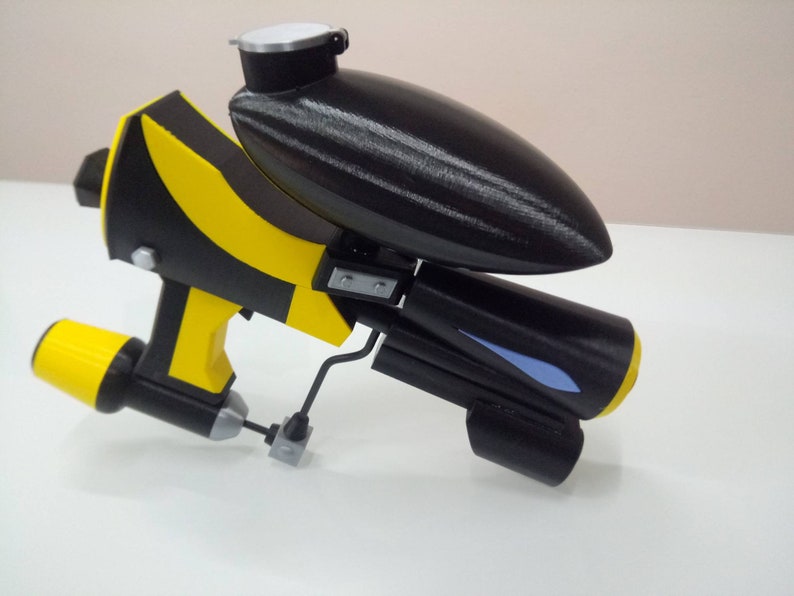 May include: A black and yellow toy gun with a blue detail. The gun has a black tank on top and a yellow barrel.