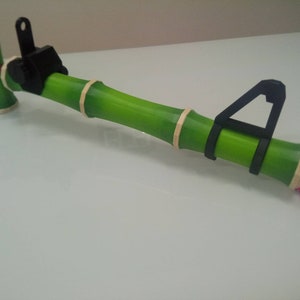 Puede incluir: Un juguete de pistola de bamb&uacute; verde con un gatillo de pl&aacute;stico negro y un mango de pl&aacute;stico negro. La pistola tiene un c&iacute;rculo rosa unido al extremo.