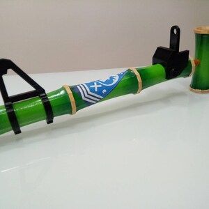Puede incluir: Una pipa de bamb&uacute; verde y negra con un dise&ntilde;o azul y blanco. La pipa tiene un accesorio de metal negro en el extremo.