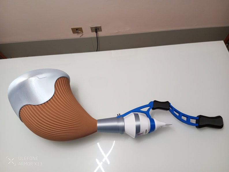 May include: A brown and silver 3D printed object with a blue and black plastic handle. The object is shaped like a horn and has a white tube attached to it.