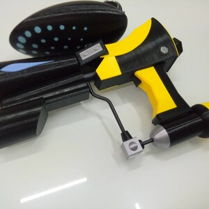 May include: A black and yellow toy gun with a blue and white detail on the side. The gun has a black handle and a silver trigger.