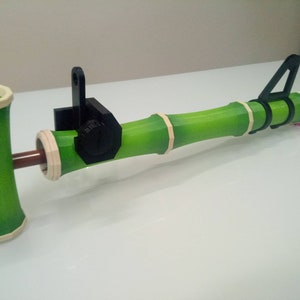 Puede incluir: Un juguete de bamb&uacute; verde con un mango de pl&aacute;stico negro y una clavija de madera marr&oacute;n. El juguete est&aacute; dise&ntilde;ado para ser utilizado como un lanzador de proyectiles.