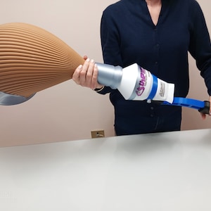 May include: A person holding a blue and white dust removal tool with a long, brown, pleated extension. The tool has a handle and a white, round, dust-catching head with the word "SHARP" printed on it.