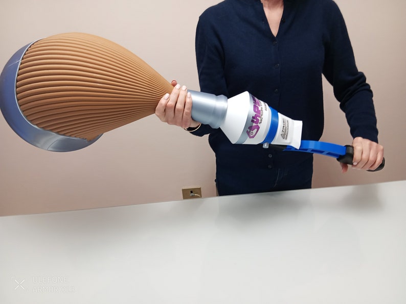 May include: A person holding a blue and white dust removal tool with a long, brown, pleated extension. The tool has a handle and a white, round, dust-catching head with the word "SHARP" printed on it.
