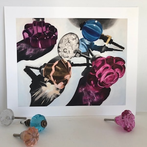 May include: A collection of vintage glass door knobs in various colors and styles, including pink, purple, blue, and gold. The knobs are arranged on a white background and cast shadows.