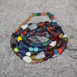 Könnte beinhalten: Eine mehrreihige Halskette aus bunten Glasperlen in Blautönen, Grün, Rot, Gelb und Weiß. Die Perlen sind in verschiedenen Größen und Formen, was ein einzigartiges und auffälliges Design ergibt.