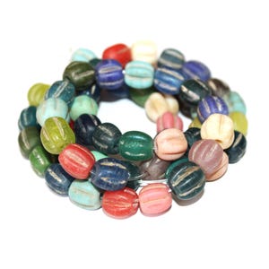 Könnte beinhalten: Eine Kette aus bunten, oval geformten Perlen in verschiedenen Farben wie Rot, Blau, Grün und Creme. Jede Perle hat ein gestreiftes Design. Die Perlen sind aufgereiht und bilden eine kreisförmige Form vor weißem Hintergrund.