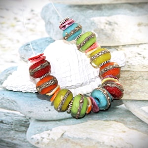 Peut inclure: Un collier de perles colorées avec une variété de couleurs, notamment le rouge, l'orange, le jaune, le vert, le bleu et le turquoise. Les perles sont rondes et ont une finition métallique. Le collier est enfilé sur un cordon transparent.