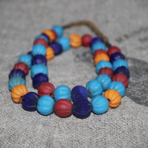 Könnte beinhalten: Eine Halskette aus blauen, orangen und roten Glasperlen. Die Perlen sind rund und haben eine leicht strukturierte Oberfläche.