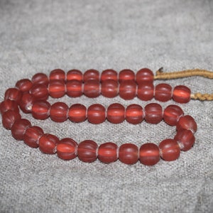 Könnte beinhalten: Eine Kette aus roten Glasperlen mit einer braunen Schnur. Die Perlen sind rund und haben eine strukturierte Oberfläche.