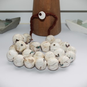 Peut inclure: Un ensemble de perles blanches cassé à motifs, avec un cordon marron et une base en bois. Les perles sont disposées en cercle. Une perle blanche en forme d'œil est attachée au cordon marron.