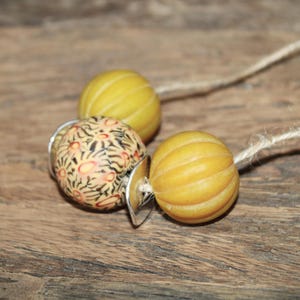 Könnte beinhalten: Eine Halskette mit drei Perlen, eine mit einem gelben und weißen Streifenmuster, eine mit einem gelben und weißen Streifenmuster und eine mit einem schwarzen und orangefarbenen Blumenmuster.