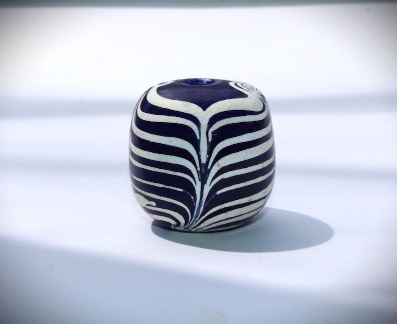 May include: A blue and white glass bead with a swirling pattern. The bead is round and has a hole in the center.