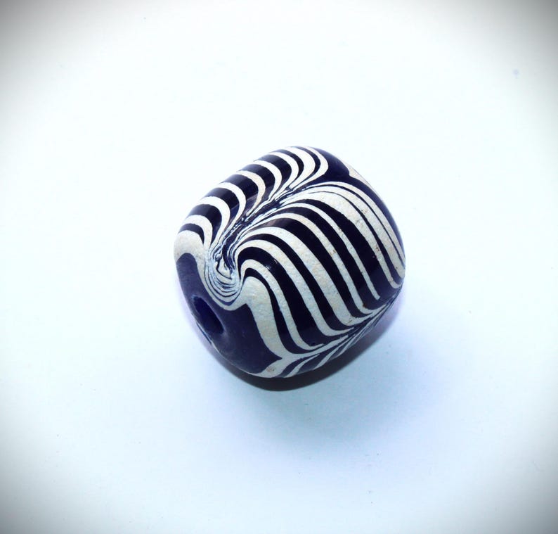 May include: A white and blue glass bead with a swirling, striped pattern. The bead is round and has a hole in the center.