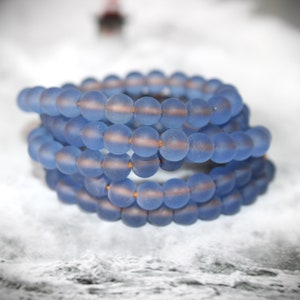 Op de afbeelding: Een stapel blauwe glazen kralen armbanden. De kralen zijn mat en hebben een subtiele glans.