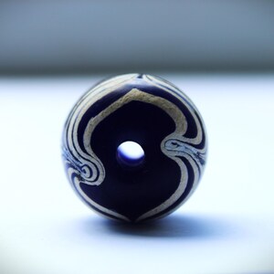 May include: A blue and white glass bead with a swirling pattern. The bead has a hole in the center for stringing.