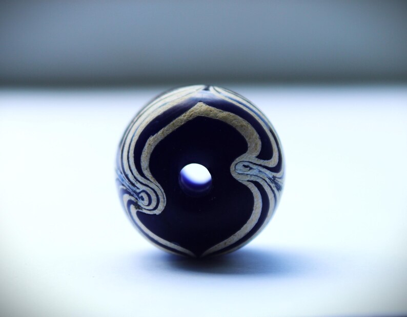 May include: A blue and white glass bead with a swirling pattern. The bead has a hole in the center for stringing.