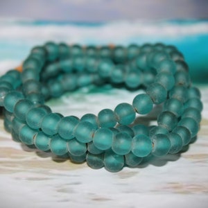 May include: A strand of teal blue glass beads, layered and knotted together, creating a simple and elegant necklace.