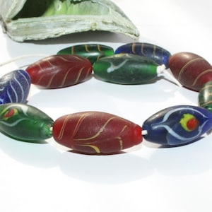 Könnte beinhalten: Eine Kette aus bunten Glasperlen mit wirbelnden Mustern. Die Perlen sind oval geformt und haben eine Mischung aus roten, grünen und blauen Farben.