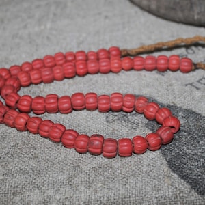 Könnte beinhalten: Eine rote Perlenkette mit einer braunen Schnur. Die Perlen sind rund und haben eine strukturierte Oberfläche.