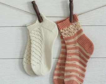 May include: Two pairs of knitted socks hanging on a clothesline. One pair is white with a lacy pattern, and the other pair is peach with a striped pattern.