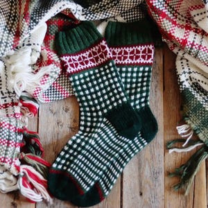 Könnte beinhalten: Ein Paar grüne und weiße gemusterte Socken mit einem roten und weißen Streifen. Die Socken liegen auf einer karierten Decke.