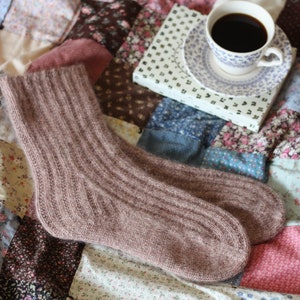 Könnte beinhalten: Ein Paar braune Stricksocken auf einem Patchwork-Deckenstück mit einer Tasse Kaffee und einem Buch.