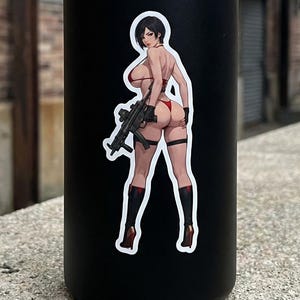 May include: Black insulated water bottle with a sticker featuring a female anime character in a red bikini holding a rifle. The sticker has a white border and is affixed to the front of the bottle.