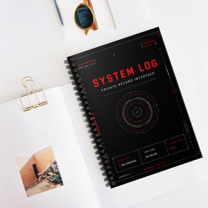 Op de afbeelding: Een zwart spiraalgebonden notitieboek met de woorden "SYSTEM LOG" in het rood. De omslag heeft een cirkelvormige afbeelding en de tekst "PRIVATE RECORD INTERFACE". Extra tekst omvat "RECORDING", "TIME STAMP 23:59:59" en "ACCESS LEVEL RED".