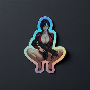 Può includere: Un adesivo fustellato raffigurante un personaggio in stile anime con capelli neri corti, che indossa un body rosso e nero, accovacciato mentre impugna un mitra nero. L'adesivo ha una finitura olografica che riflette la luce in tonalità blu e arancioni.