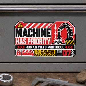 Może przedstawiać: Prostokątna naklejka w kolorach czerwonym, czarnym i białym, przedstawiająca ramię robota i postać ludzką. Tekst zawiera napisy MACHINE HAS PRIORITY, HUMAN YIELD PROTOCOL, DO NOT RESIST AUTOMATION oraz SECTOR 07, wraz z ikonami ostrzegawczymi.