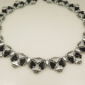 May include: A silver and black beaded necklace with a geometric pattern. The necklace is made of small, triangular beads arranged in a repeating design.