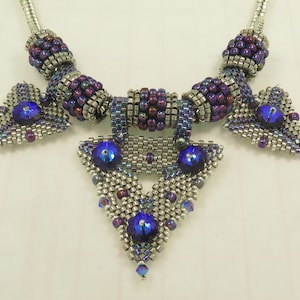 May include: A silver and purple beaded necklace with a geometric pendant featuring blue crystals.