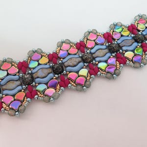 May include: A beaded bracelet with a colorful, iridescent design. The bracelet features a repeating pattern of pink, blue, and iridescent beads, with dark gray and red accents. The bracelet is set against a white background.